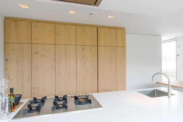 Houten kastenwand met schuifdeur achter het witte keukenblok