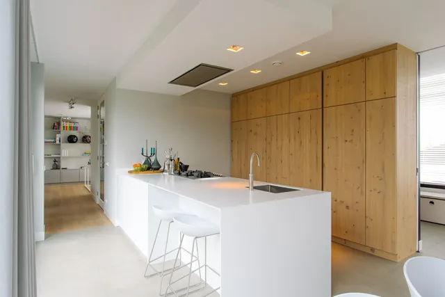 Witte keuken met kookeiland en een hoge kastenwand van licht hout