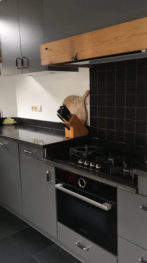 Gerenoveerde keuken met donkere fronten en een houten afzuigkap